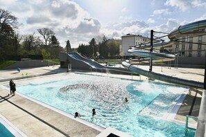 A swimming pool with a water slide, surrounded by a concrete deck and trees. - Villa Thermae Nancy (Nancy)