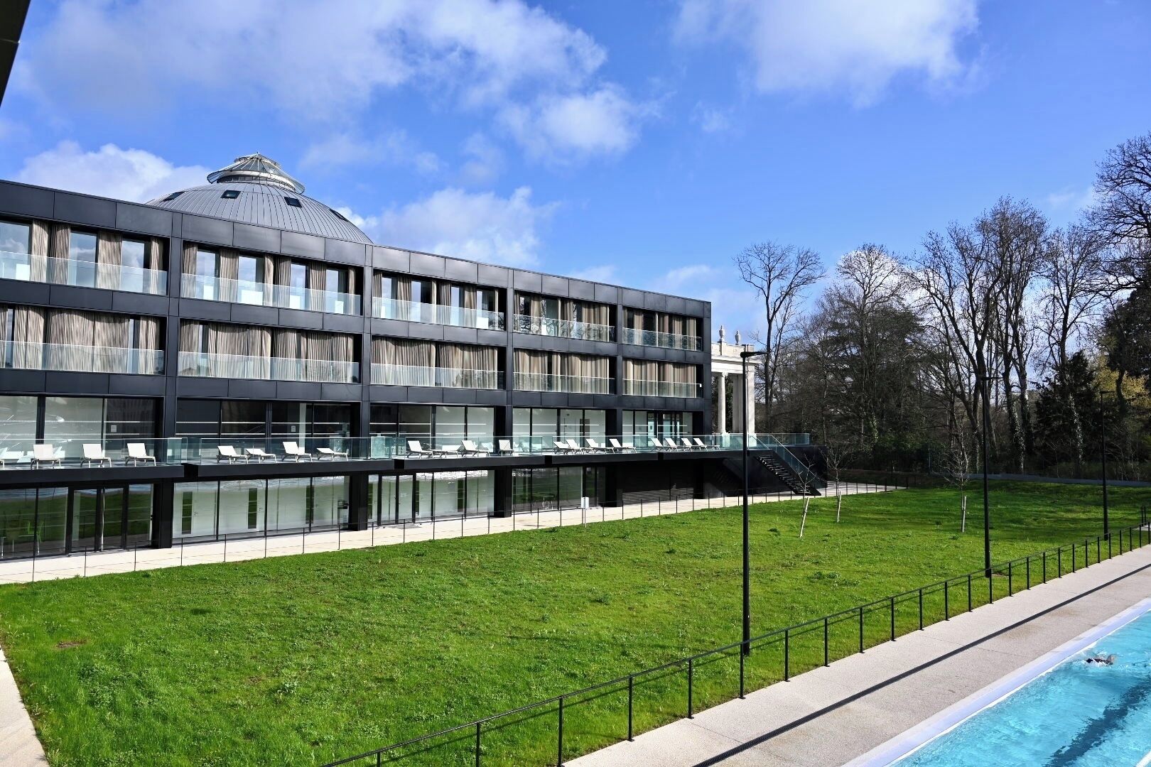 Un edificio moderno con fachada de vidrio, piscina y zona verde.