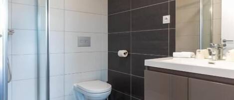 Un baño moderno con cabina de ducha de vidrio, inodoro y tocador con espejo.