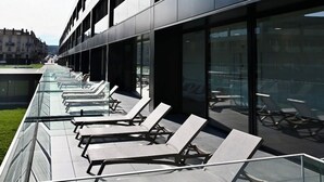 A modern building with multiple floors, large glass windows, and outdoor seating areas with sun loungers. - Villa Thermae Nancy (Nancy)
