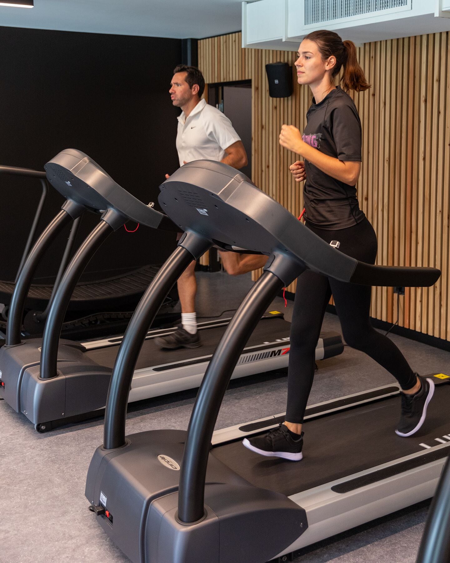A gym with treadmills and a wooden wall in the background.