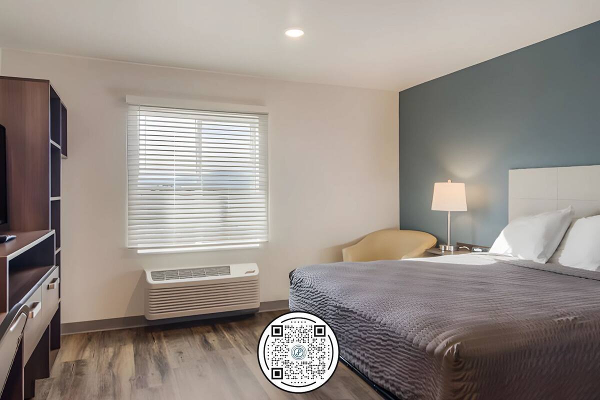 Une chambre d’hôtel comprenant un lit, une télévision, une fenêtre avec des stores, un bureau avec une lampe et une chaise.