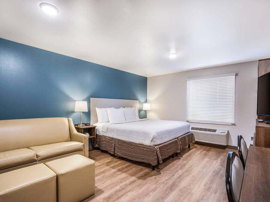 Een hotelkamer met een bed, een sofa, een bureau en een raam met jaloezieën.