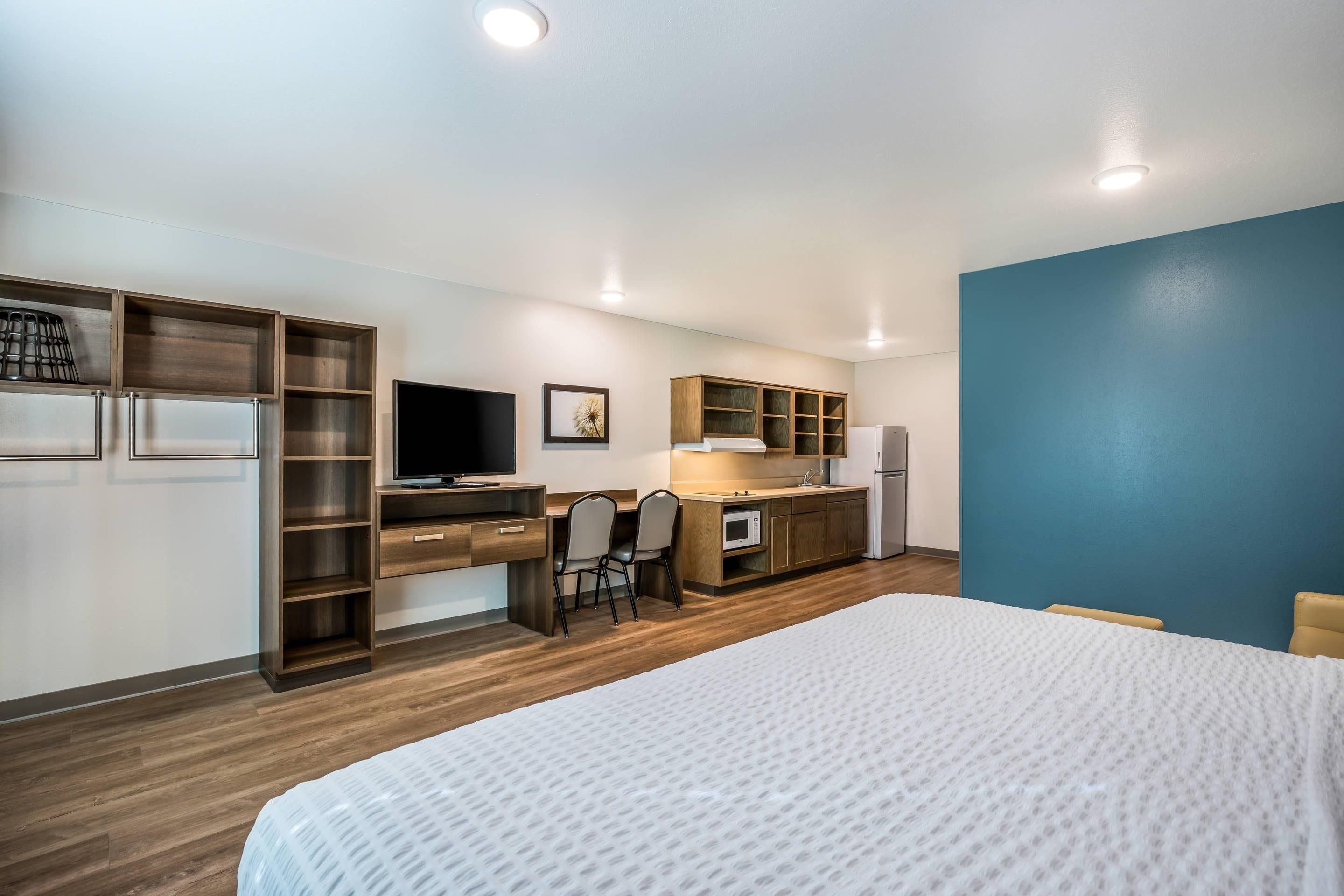 A hotel room with a bed, a desk with a computer, a microwave, and a refrigerator.