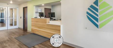 A reception area with a wooden reception desk, a computer, and a flat-screen TV. There is a glass door leading to another room.