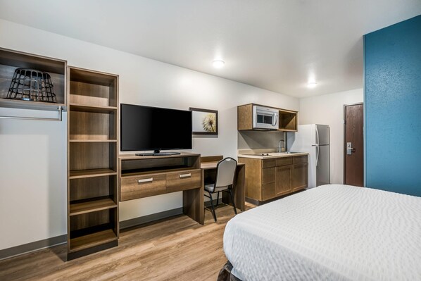 A compact hotel room with a bed, a desk with a computer, a microwave, a refrigerator, and a small kitchenette. - Woodspring Suites Downers Grove - Chicago (Downers Grove)