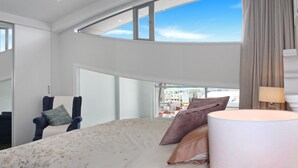 Une chambre d’hôtel moderne, dotée d’un grand lit, d’une chaise, d’une lampe et offrant une vue sur la ville grâce à de grandes fenêtres.