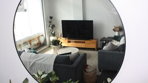 Un salon avec un canapé, une table basse, un téléviseur posé sur un meuble en bois et une plante en pot.