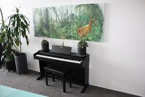 Guests can enjoy relaxing in this serene room, featuring a black piano, two potted plants, and a beautiful framed painting.