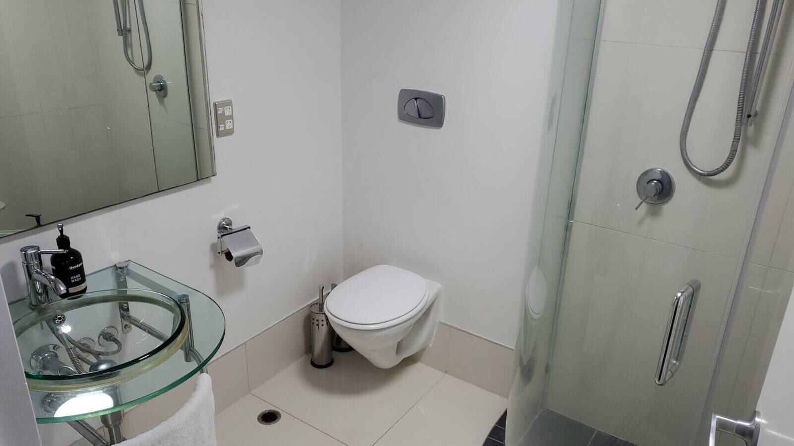Een moderne badkamer met een glazen wastafel, toilet en douche.