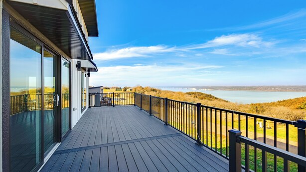 Eine Holzterrasse mit Glastüren und Geländer, mit Blick auf Strand und Wasser.