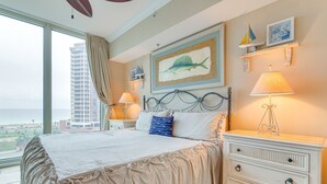 Une chambre avec un grand lit, une commode, une table de chevet et une fenêtre donnant sur un immeuble de grande hauteur.