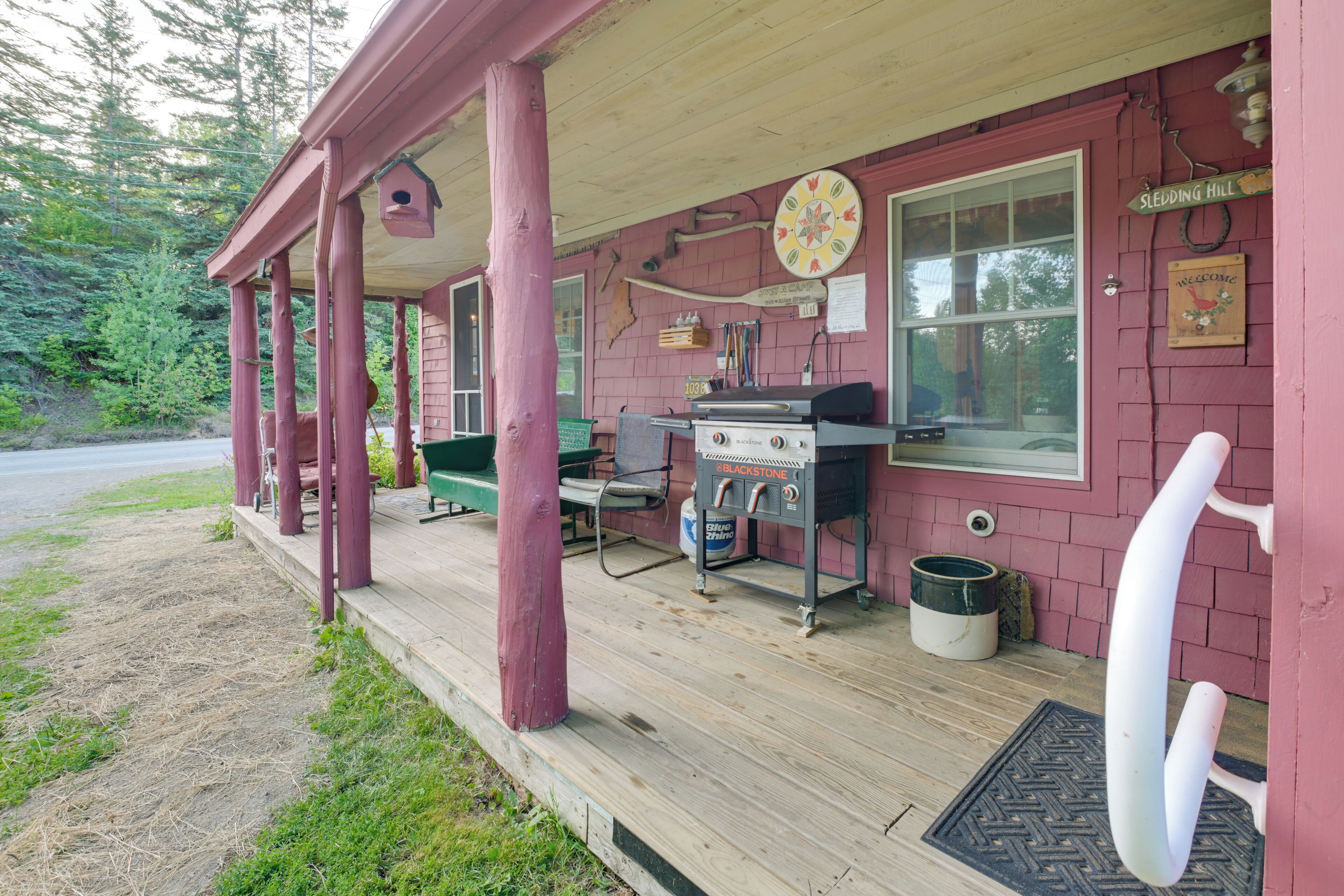A rustic cabin with a porch, a grill, and a welcome sign.