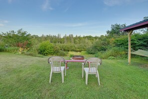 Una mesa de picnic con dos sillas en un área verde, con un bosque al fondo.