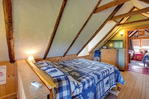 Um quarto com teto de madeira, uma cama com colcha, uma mesinha de cabeceira e um guarda-roupa.