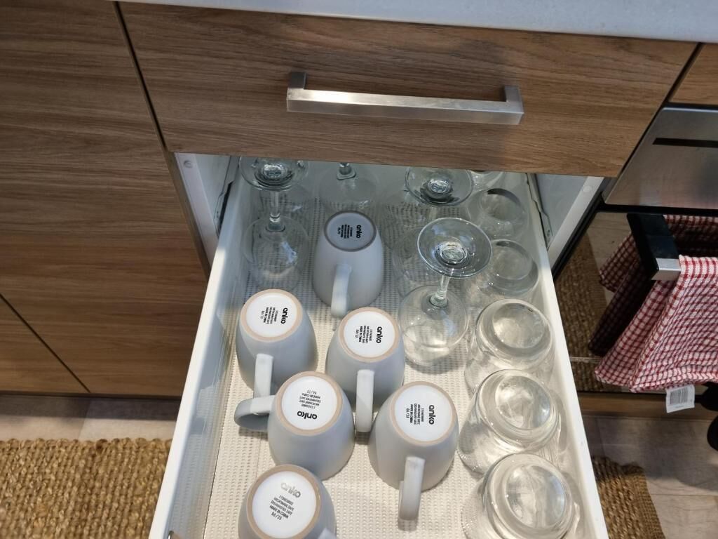 Een lade met witte keramische mokken en glazen bekers, met de merknaam 'onico' erop.