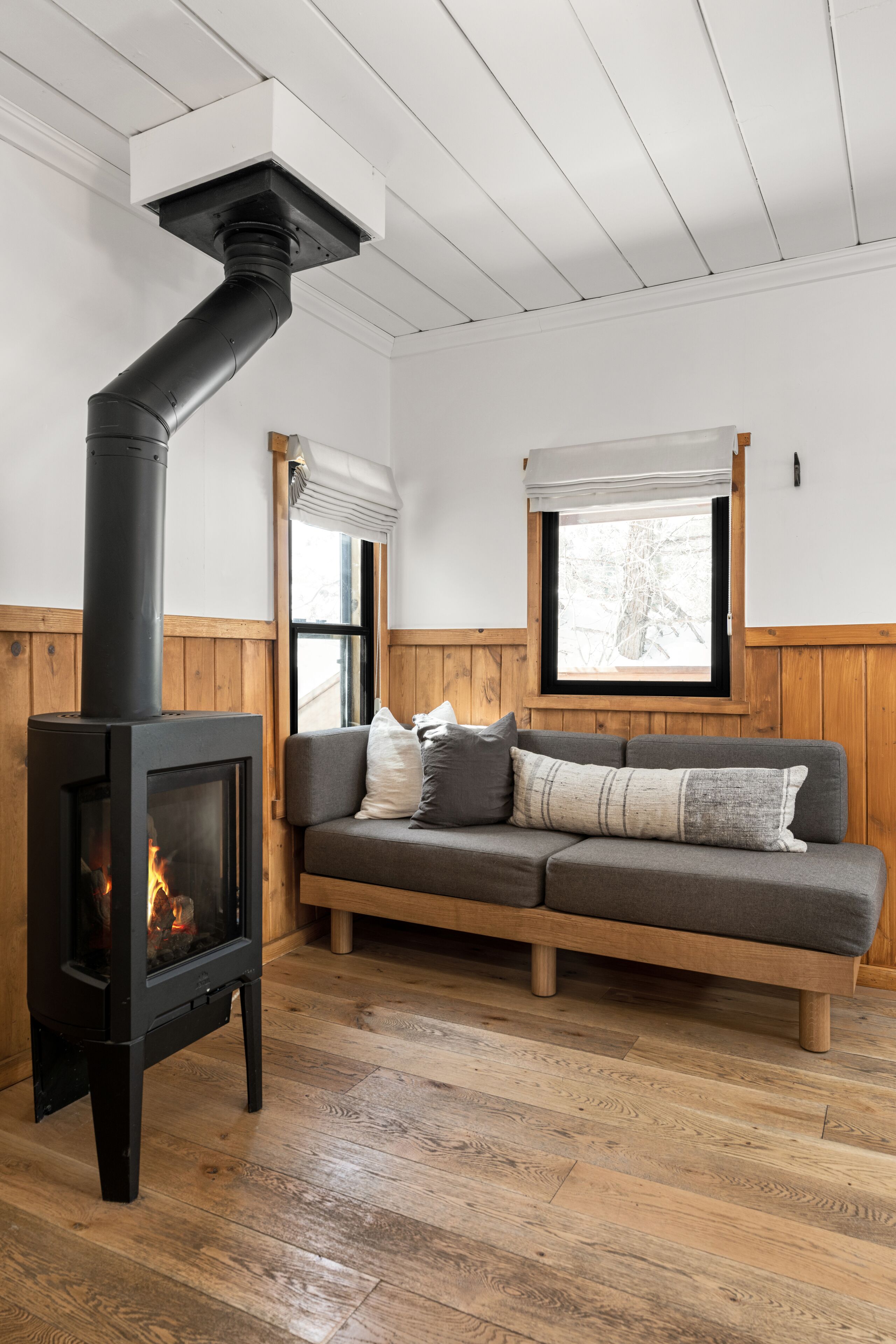 A cozy room with a wood-burning stove, a wooden bench, and a window with a view of trees.