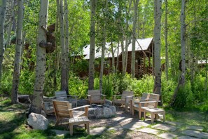 A wooden deck with chairs and a fire pit surrounded by birch trees.