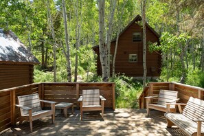 A wooden deck with benches and a cabin surrounded by trees.