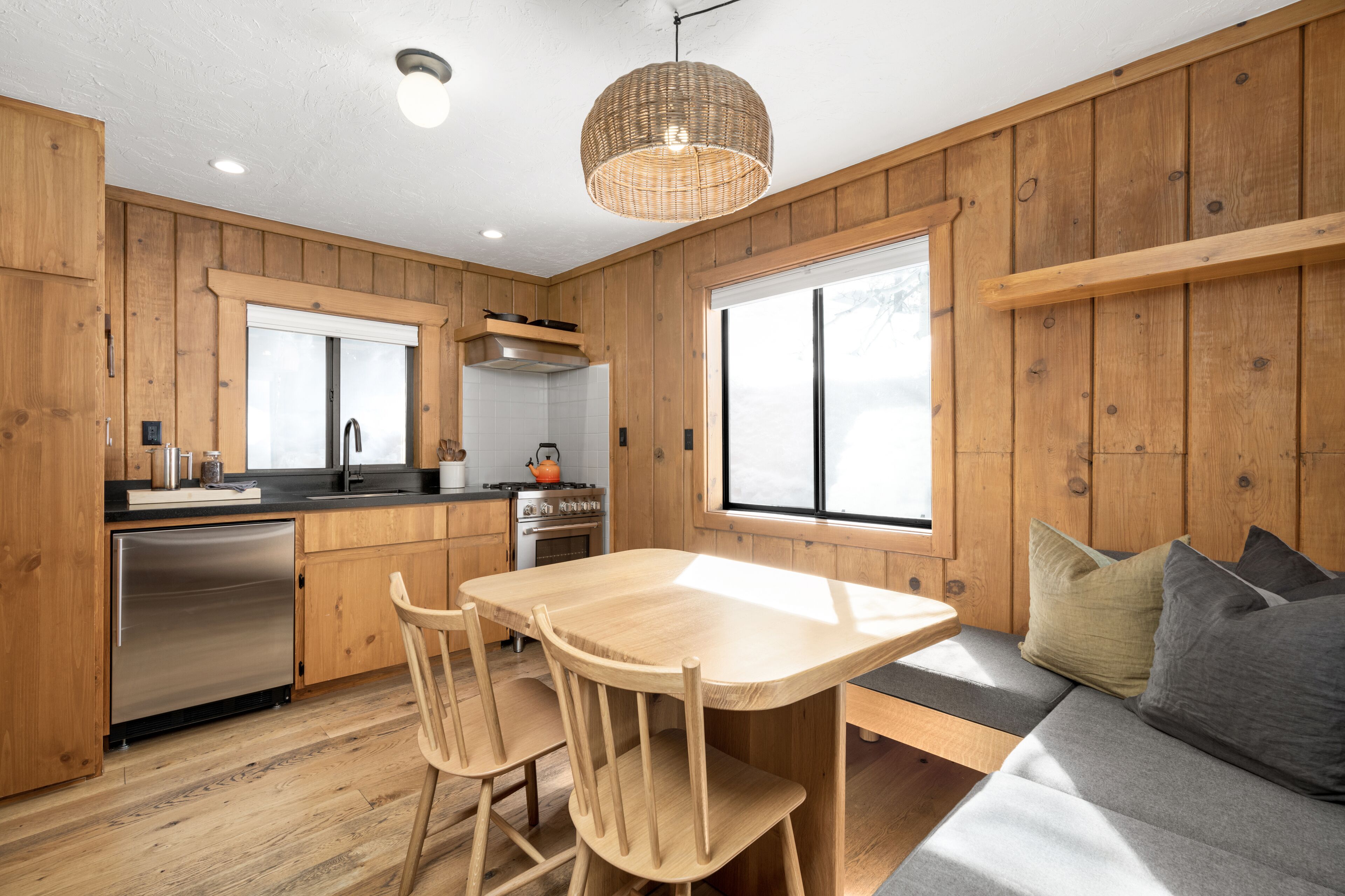Una cocina moderna con paneles de madera, un refrigerador de acero inoxidable, una mesa de comedor con sillas y un amplio ventanal que proporciona luz natural.