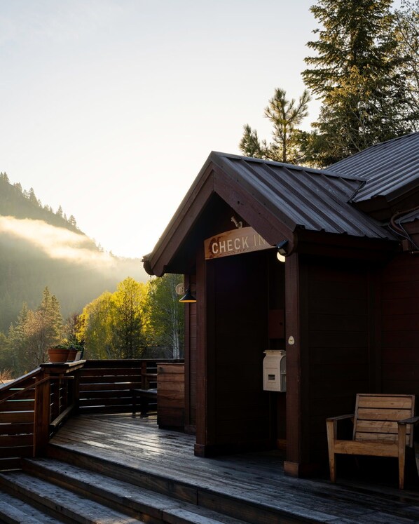 A wooden cabin with a 'CHECK IN' sign, a wooden bench, and a staircase leading up to the entrance.