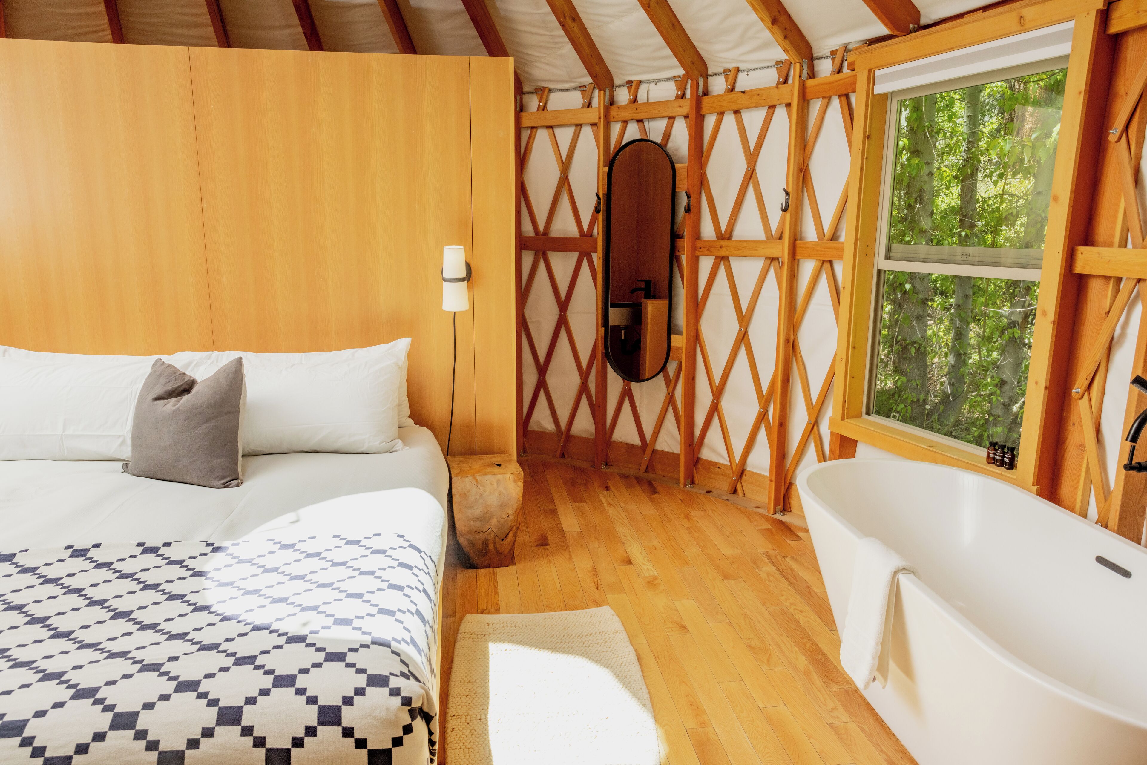 A bedroom with a large bed, a wooden wall, a window, and a bathtub.