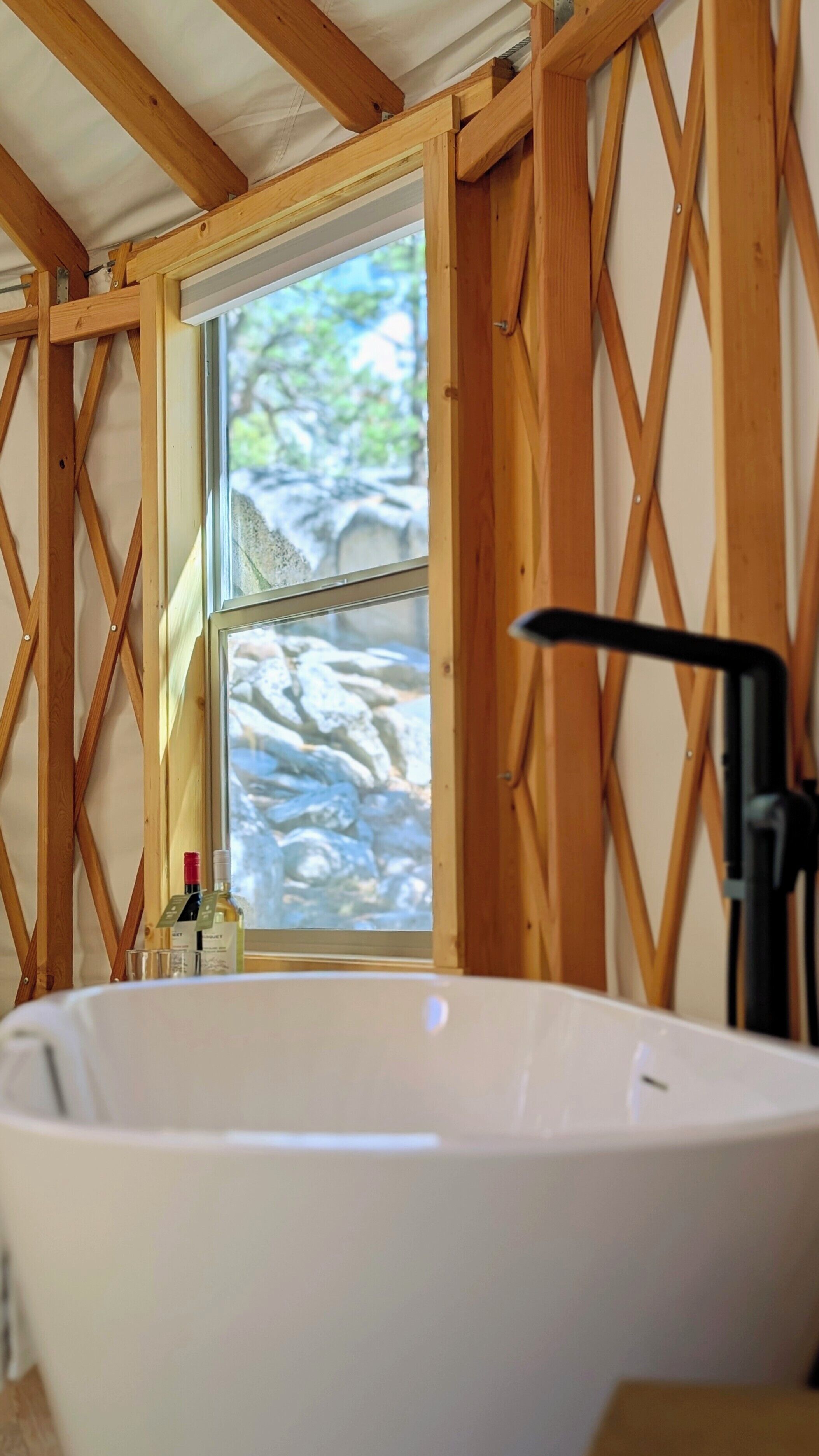 Une salle de bain dotée d’une grande baignoire, de poutres en bois et d’une fenêtre offrant une vue sur les rochers.