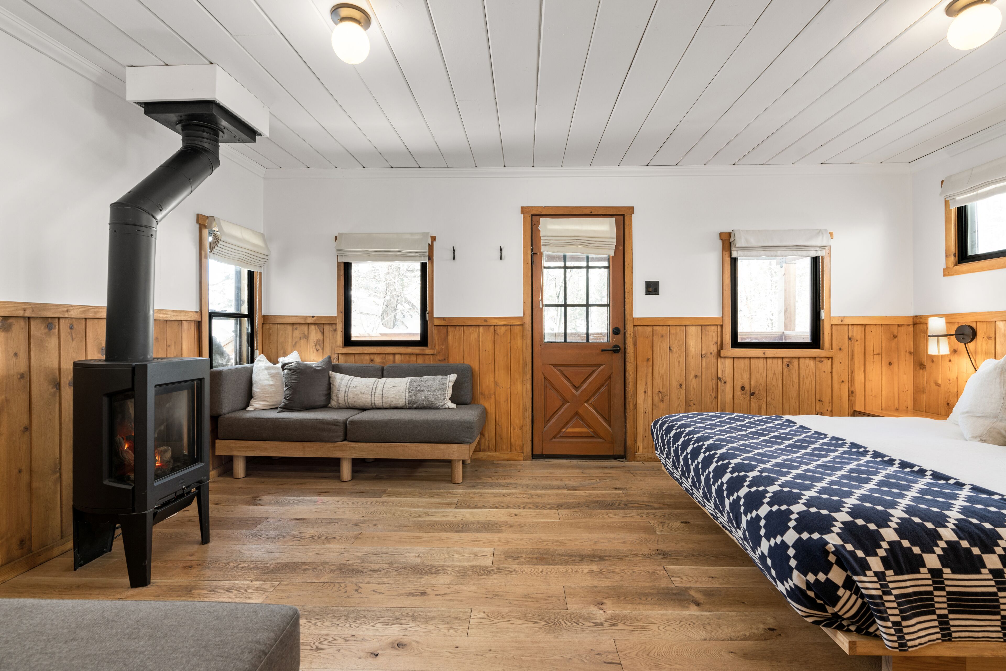 Una habitación acogedora con estufa de leña, un sofá, una cama y una puerta de madera.