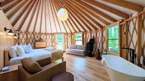 A yurt interior with a bed, sofa, and a bathtub.
