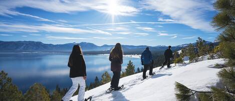 Un grupo de personas en una ladera nevada de montaña, con un lago y montañas al fondo.