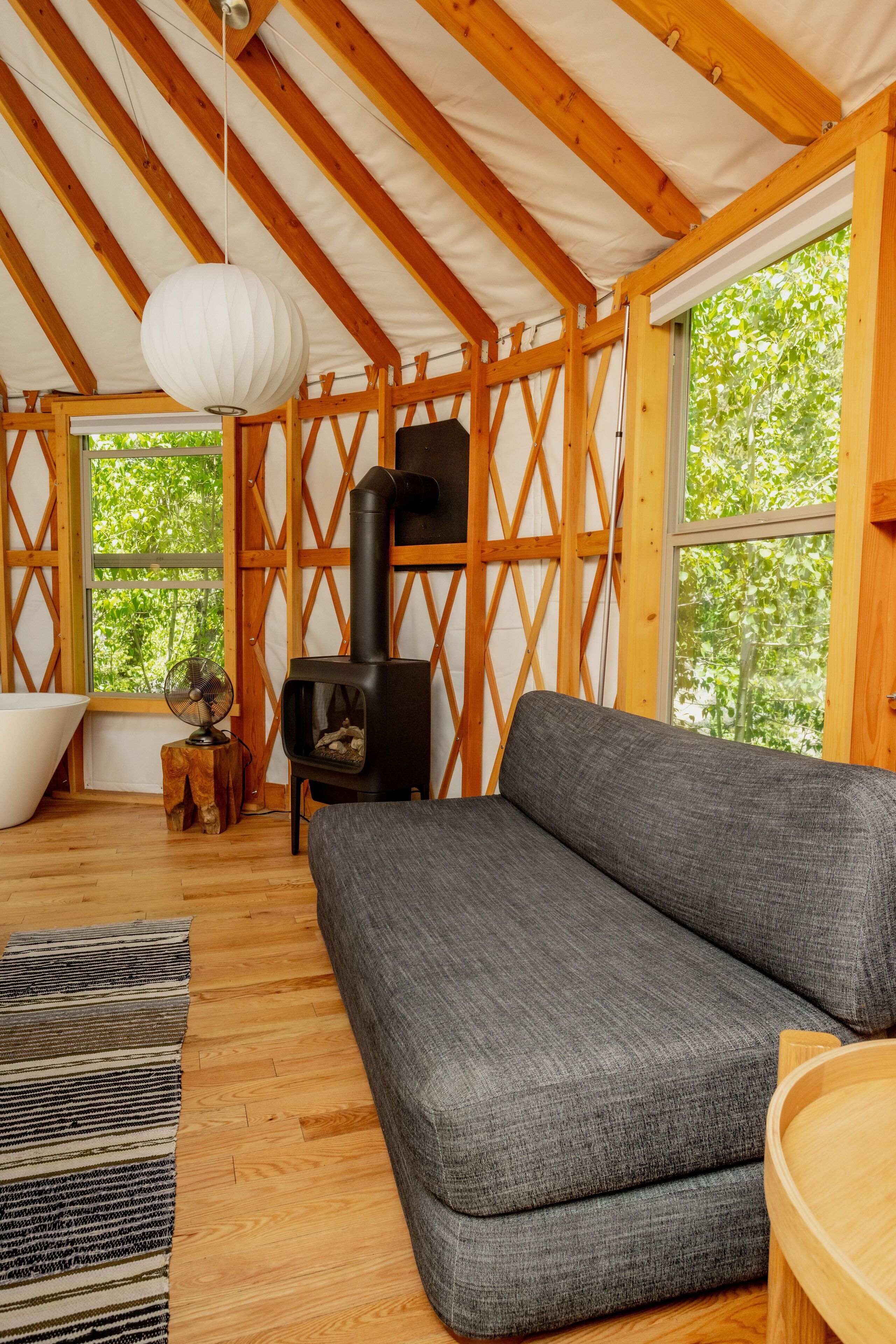 Quarto aconchegante com sofá cinza, mesa de madeira, ventilador, banheira e lareira a lenha.