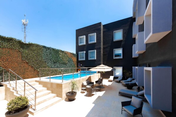 A modern outdoor pool area with a staircase leading to a building, lounge chairs, and potted plants.
