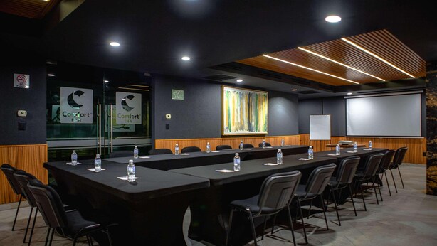 A conference room with a long table, chairs, water bottles, a projector screen, and Comfort Inn signage. - Comfort Inn Queretaro Tecnologico (Querétaro)