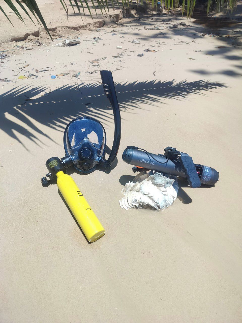 Una spiaggia sabbiosa con uno snorkel blu, una bombola d'ossigeno gialla e una macchina fotografica subacquea blu sulla sabbia.