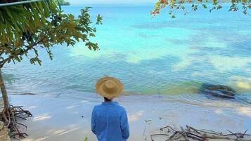 Una persona con un cappello di paglia e una camicia blu in piedi su una spiaggia sabbiosa con vista sull'oceano.