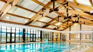 Una piscina interior amb parets de vidre transparent, bigues de fusta i vista a les muntanyes.