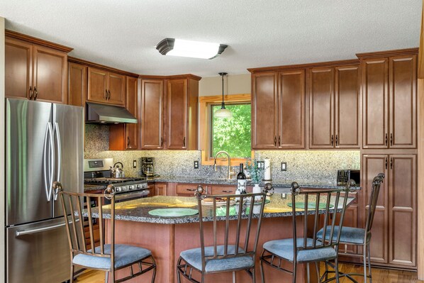 Una cocina moderna con armarios de madera, electrodomésticos de acero inoxidable y una isla central con taburetes de bar.