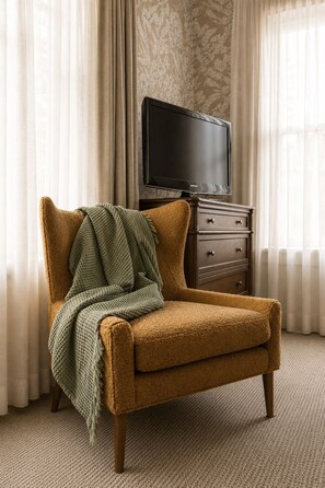 Un sillón marrón solitario con una manta verde, ubicado frente a una cómoda de madera con un televisor encima.