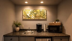 Cocina compacta con encimera de granito, lavamanos de acero inoxidable, cafetera, microondas y una planta en maceta.