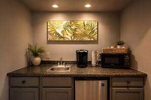 A compact kitchen with a granite countertop, stainless steel sink, coffee maker, microwave, and a potted plant. - The De La Vina Inn (Santa Barbara)