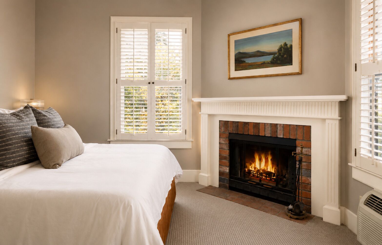 A bedroom with a bed, a fireplace, and a window with shutters.