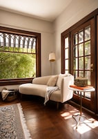 Una habitación con sofá color beige, una lámpara de pie, una mesita con un objeto decorativo y un ventanal con vistas a la vegetación.