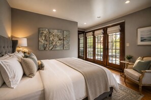 A bedroom with a large bed, a nightstand, a lamp, and artwork on the wall. - The De La Vina Inn (Santa Barbara)