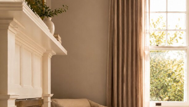 Una habitación con chimenea, un sillón, una ventana con cortinas y vistas al exterior.