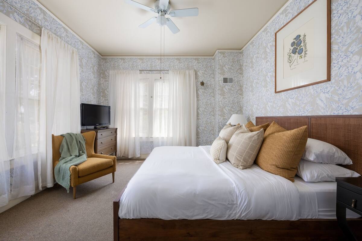 A hotel room with a bed, a chair, a television, and a ceiling fan.