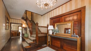 A hallway with a wooden staircase, a mirror, a lamp, and a fireplace. - The De La Vina Inn (Santa Barbara)