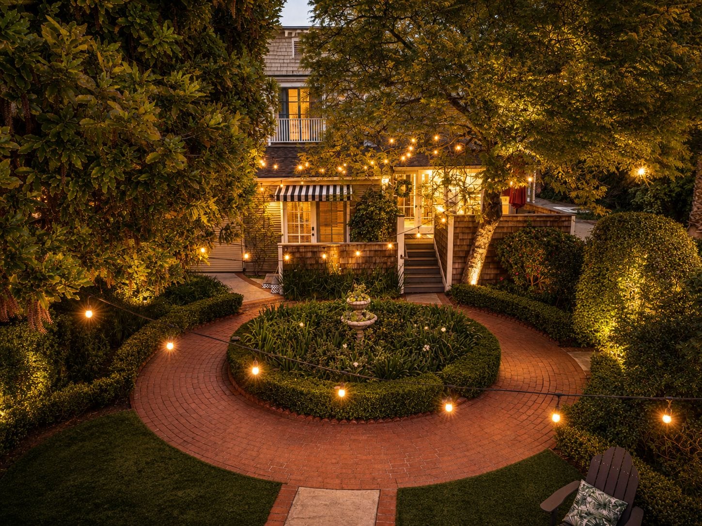 A well-lit garden with a central circular pathway, a small fountain, and a building with a balcony.