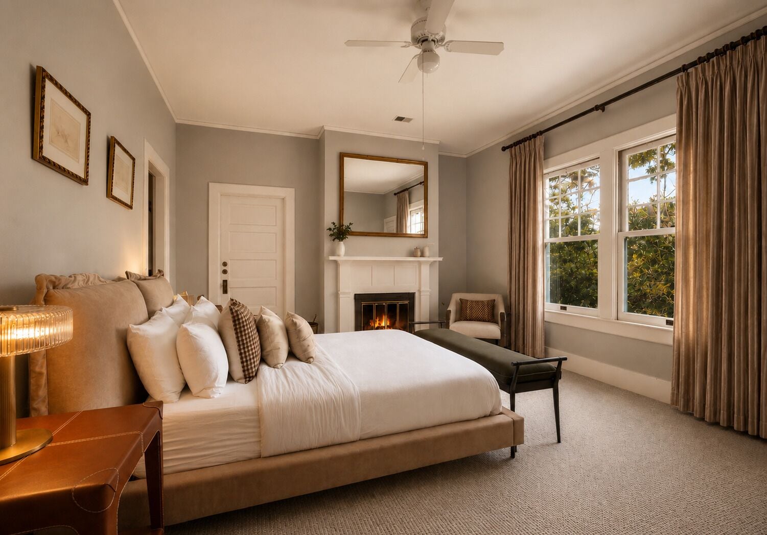 A bedroom with a large bed, a bedside table, a chair, a fireplace, and a window with curtains.