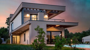 Ein modernes, zweistöckiges Haus mit Balkon, großen Fenstern und einem Pool im Vordergrund.