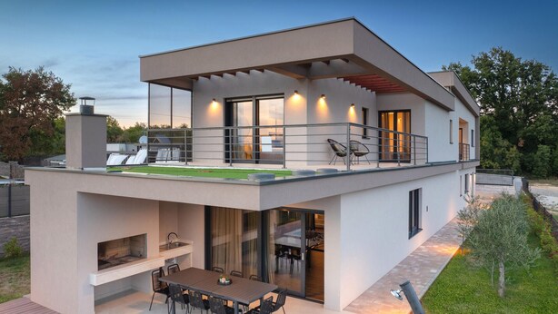 Ein modernes, zweistöckiges Haus mit Flachdach, großen Fenstern und einem Balkon.